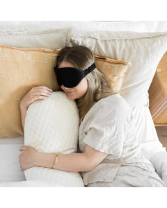 Woman resting with a pillow while wearing a black sleep mask