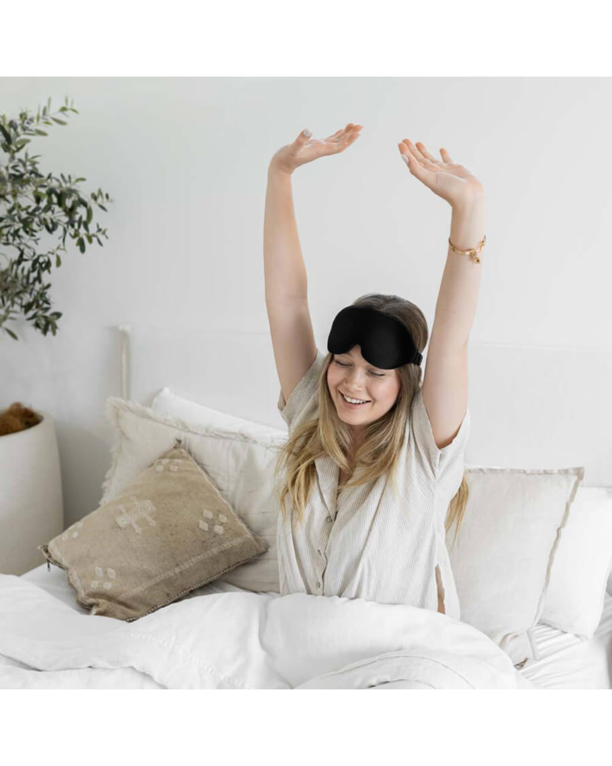 Woman stretching in bed with a black sleep mask on her forehead